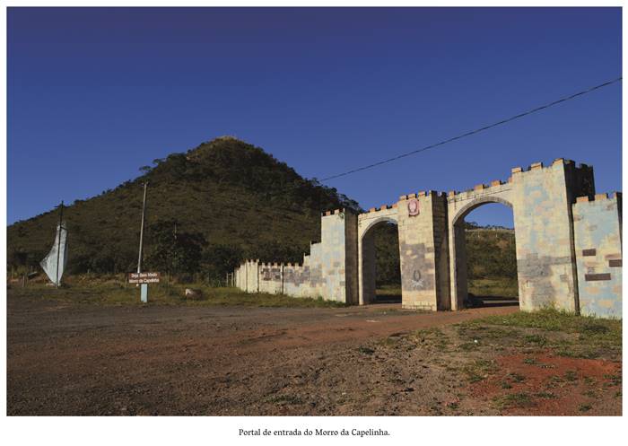  4 o- Portal de entrada do Morro da Capelinha Ao fundo o morro da Capelinha de paisagem composta por arvoredos, terras e pedregulhos. A entrada é de construção antiga na cor cinza e azul claro. Possui dois portões grandes que permanecem abertos, no alto, destacam-se torres pequenas. Realização: Academia Planaltinense de Letras, Artes e Ciências (APLAC), pelo Ecomuseu Pedra Fundamental e pelo Coletivo Nativo Audiodescrição produzida  pelo Instituto de Promoção das Pessoas com Deficiência Visual Audiodescritora: Elma Lúcia Rodrigues Consultor: Fernando Rodrigues Este projeto é promovido com recursos do Fundo de Apoio a Cultura do DF